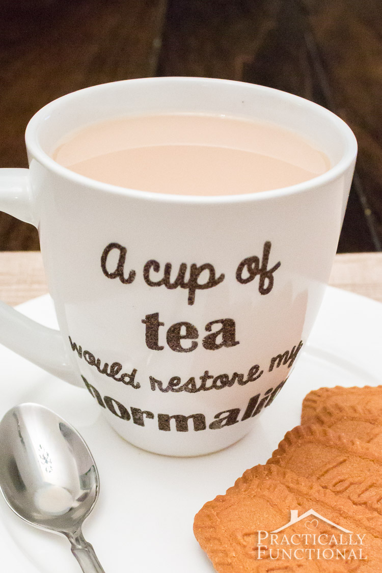 closeup of plain white ceramic mug decorated with heat transfer vinyl saying a cup of tea would restore my normality on plate with cookies and a spoon