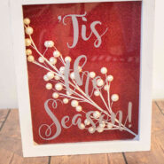 vinyl words on a shadowbox filled with glitter paper and a faux holiday berry sprig