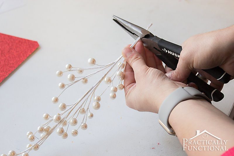 hands using wire clippers to trim stem end of faux berries sprig