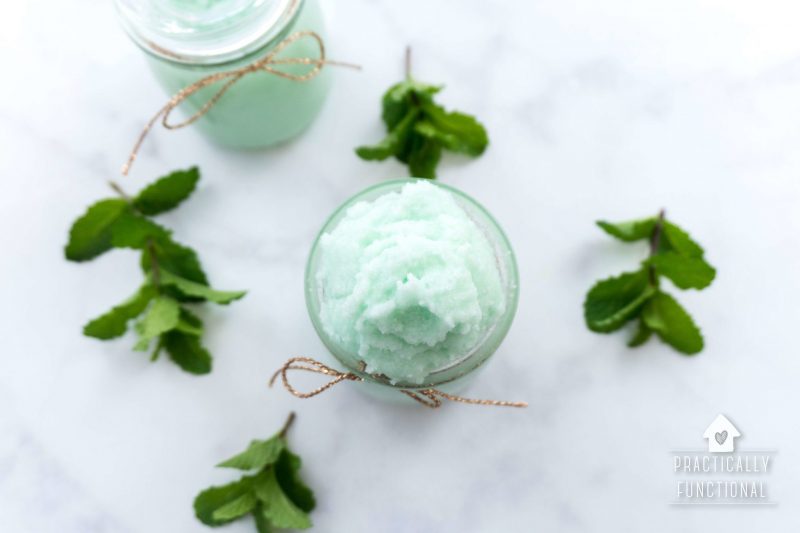 top view of homemade mint sugar scrub in two glass jars on marble countertop with mint leaves