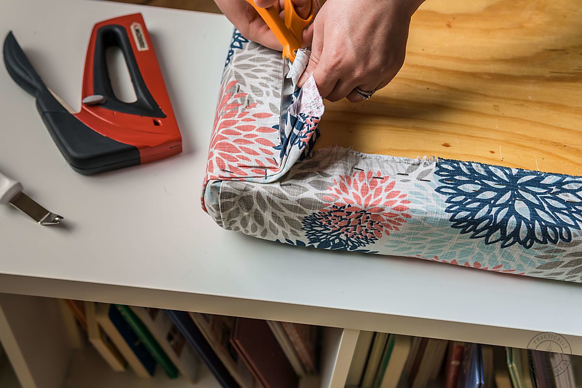 woman cutting excess upholstery fabric off back of diy bench cushion