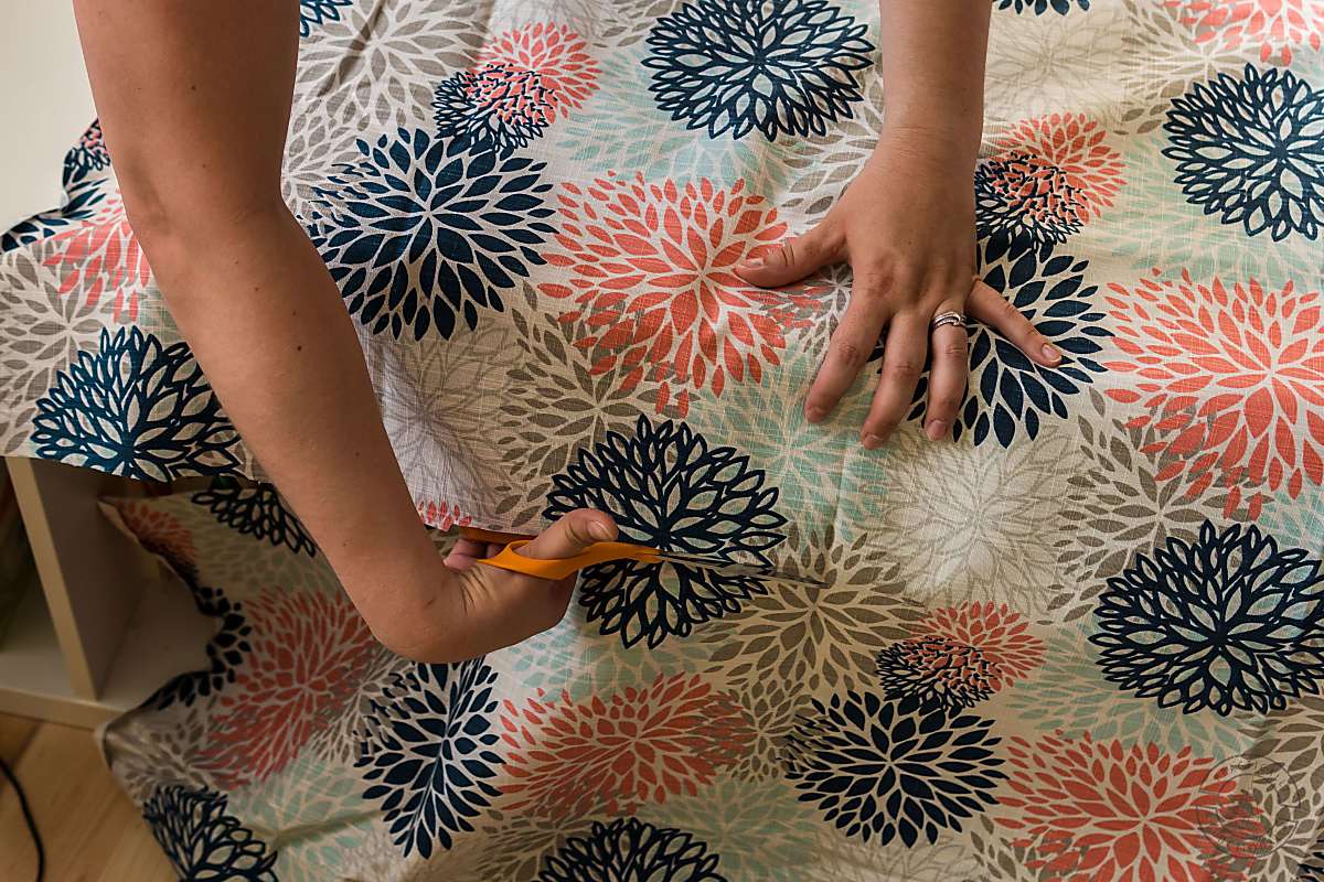 woman trimming upholstery fabric with scissors on top of a diy bench cushion