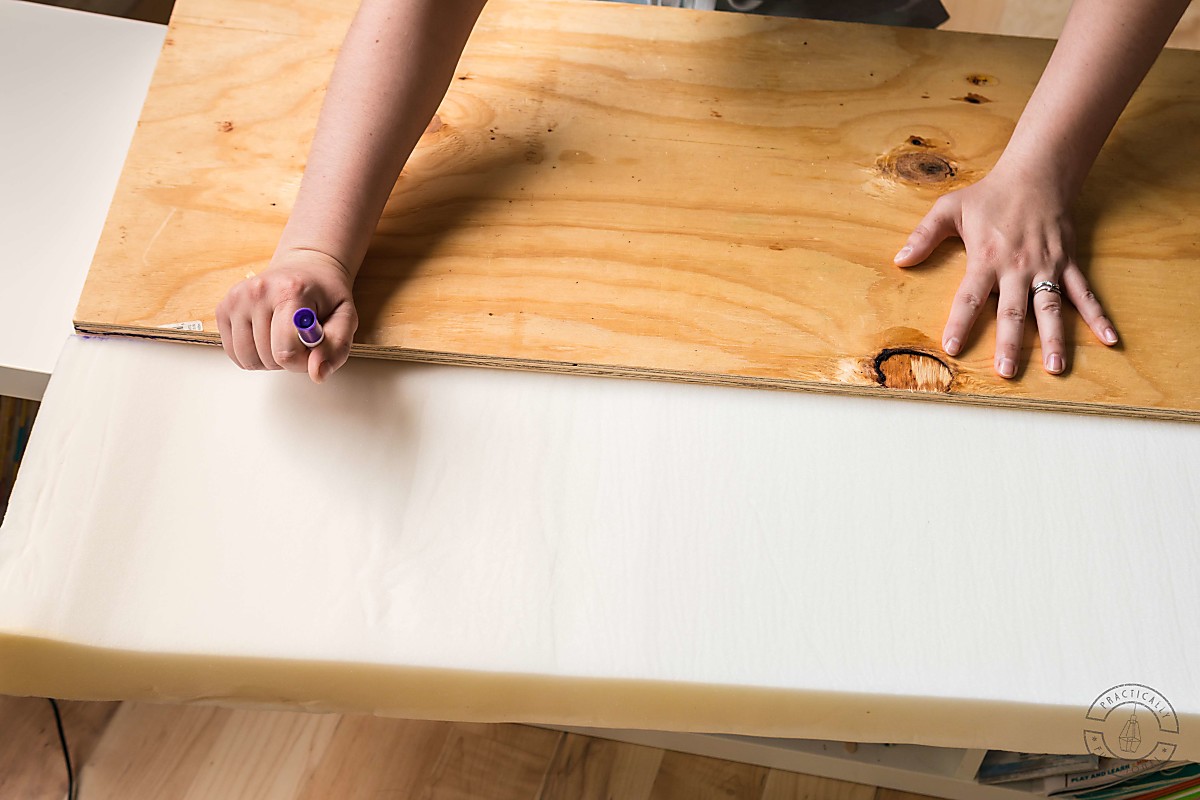 plywood on top of 3" bench foam with woman marking the edges of the wood with a marker